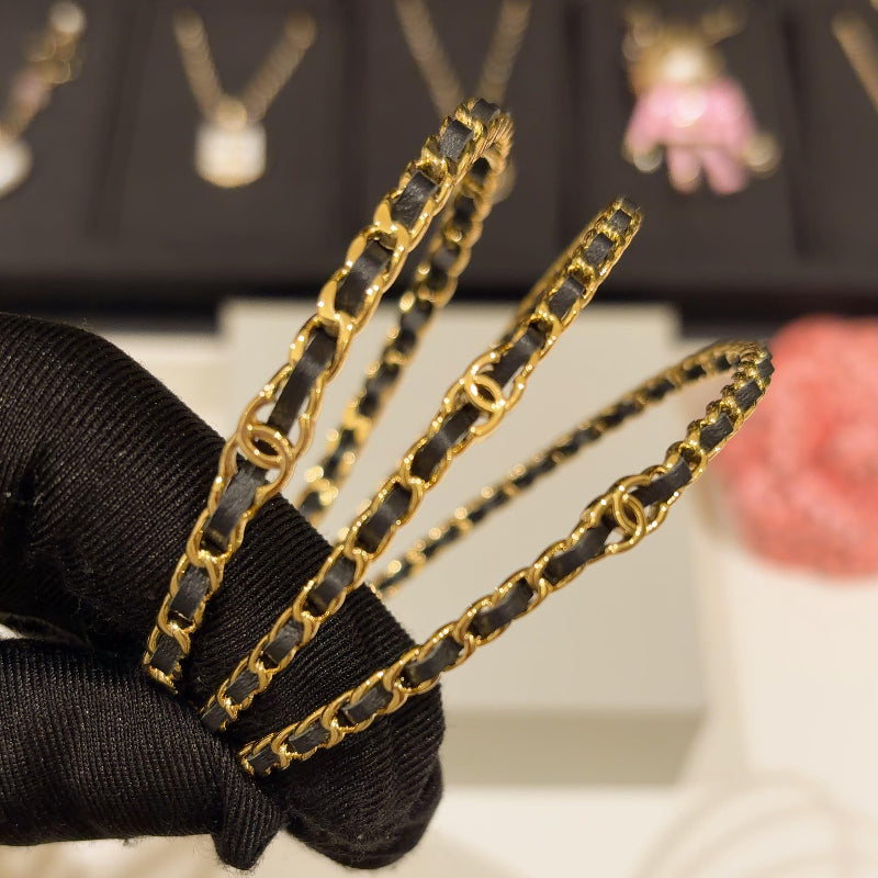 close up of CC black leather interwoven through gold chain on three stackable bangles